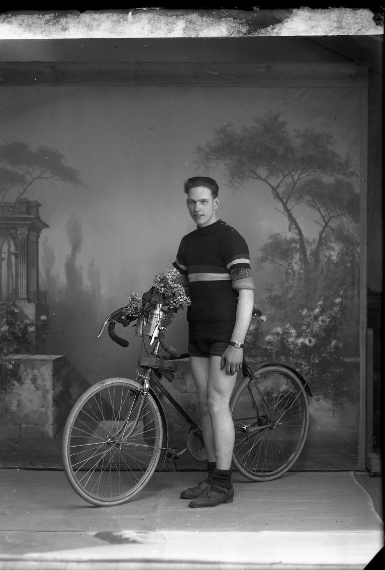 En ung man - "Bennett" - tävlingscyklist i cykelkläder med en racercykel. I vattenflaskorna vid styret sitter det blommor. Ateljébild.