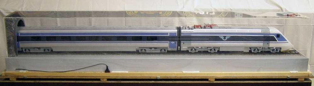 Modell av X2000 som kommer ut genom en tunnelöppning. Avtagbar monterhuv i plexiglas (Måtten 2220x310x430 avser monter.)

Modellen demonstrerar X2000-tågets speciella korglutning. Har tillhörande frakt/förvaringslåda. 

Modell/Fabrikat/typ: Elmotorvagnmodell X2000