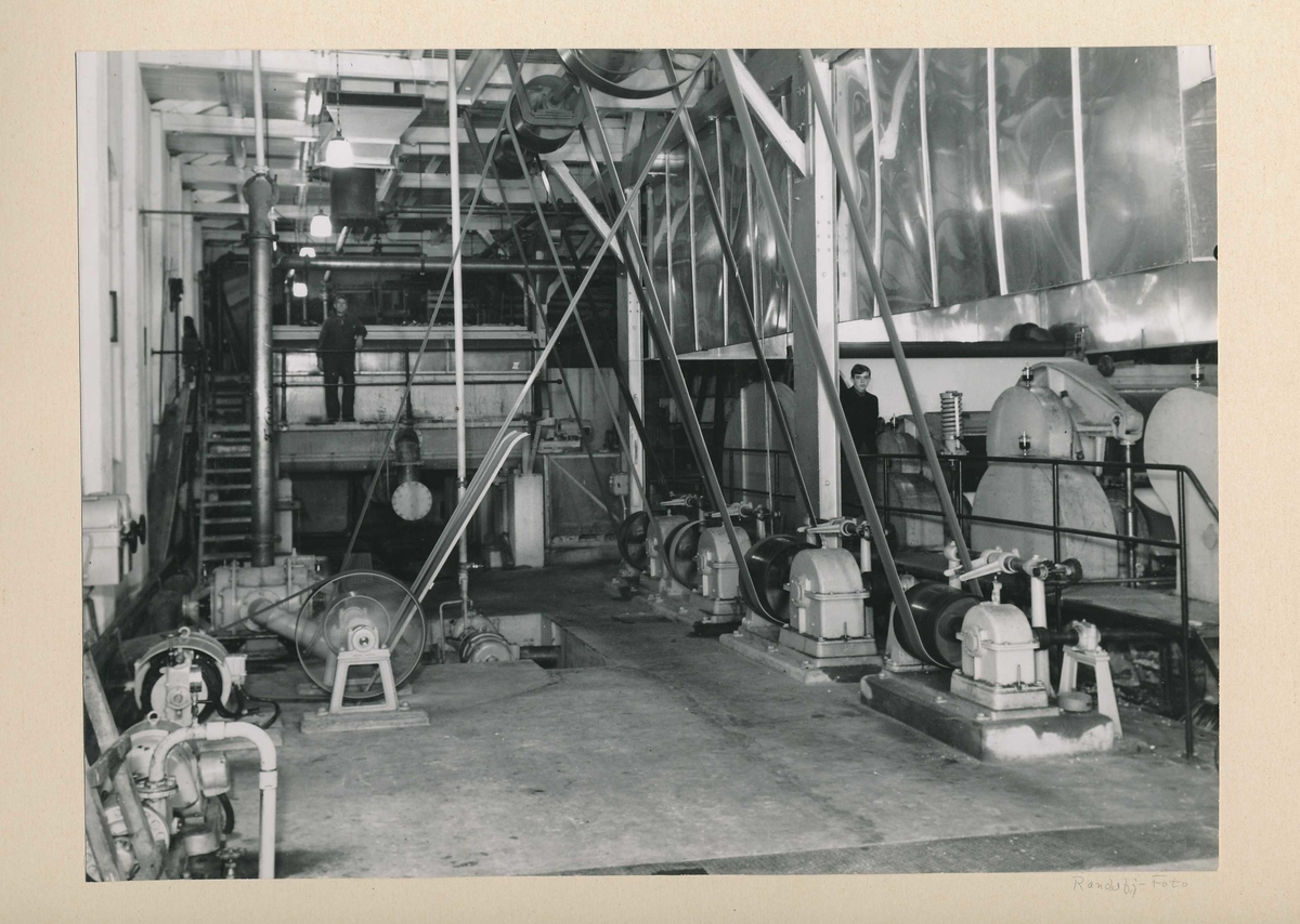 En gutt ved oppfangermaskinen og en mann ved fortykkerne i produksjonssalen i det gamle tresliperiet.
