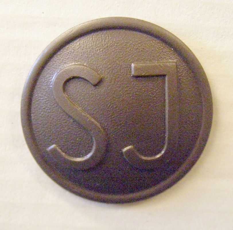 Brun rockknapp av koppar, med SJ:s logga i form av enkla initialer.