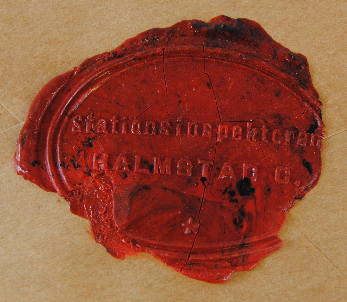 Sigillavtryck av rött lack på brunt papper. Avtrycket är format som en liggande oval. Längst ned i mitten finns en stjärna i relief.