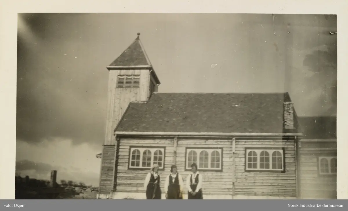 Tre damer i bunad foran langsiden til Møsstrond kirke på Hovden