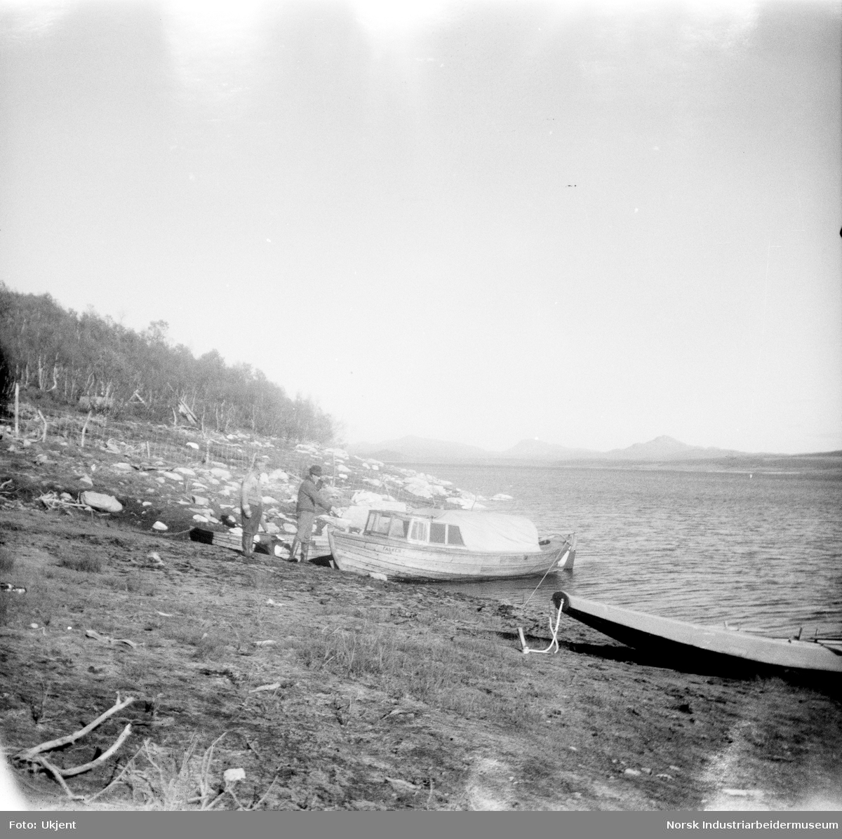 Olav O. Vågen og Trygve O. vågen ved båten "Falken" som tilhører Trygve. Båten ligger i vannkanten ved siden av en pråm på Øst-Førnes, Møsstrond