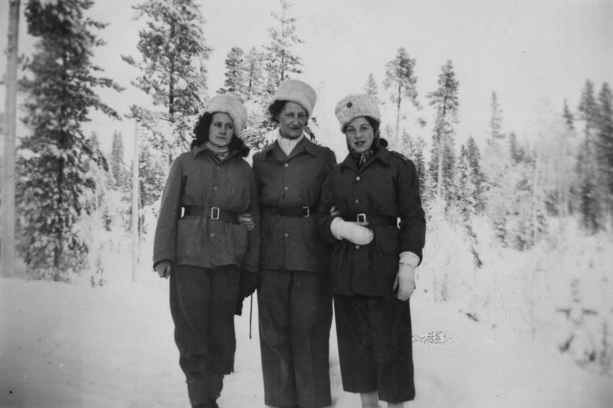 Porträttfoto av tre kvinnliga luftbevakare stående utomhus vintertid, 1942. Klädda i uniform. Från vänster Birgit Johansson, Valborg Holmberg, Karin Nordberg. Luftbevakarna tillhörde 91:a ls-kompaniet i Tellejåkk, Kåbdalis under beredskapsåren.