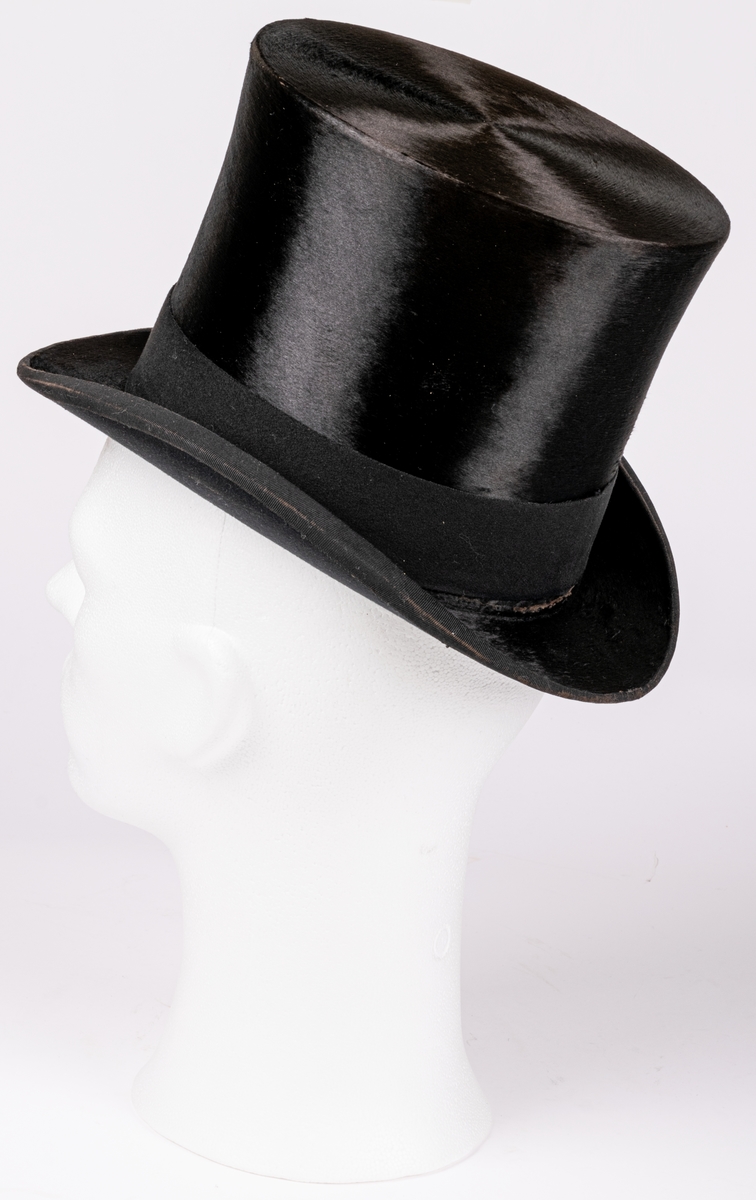 Hög hatt med kraftigt uppsvängda brätten, märkt B.L. ink. hos firma J.W. Haglund, Gefle.
Tillhörande hattask.
