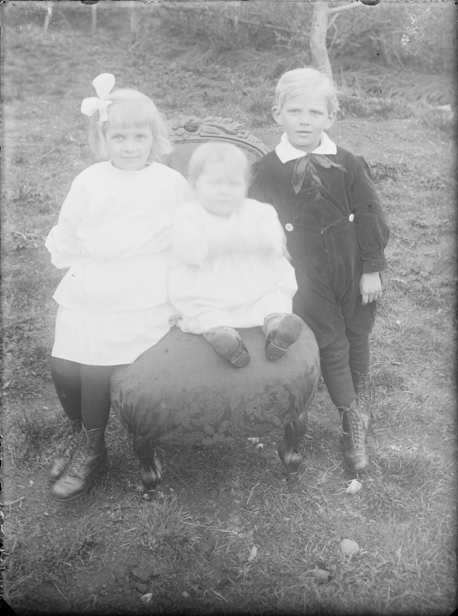 Tre barn sitter på en pall i trädgård, Alunda, Uppland