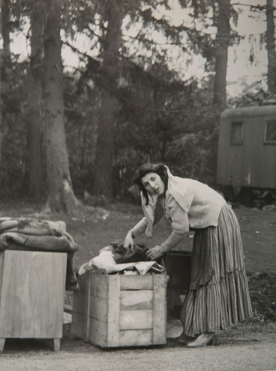 Bilden föreställer en romsk kvinna i färd med att packa inför flytten från Mälarhöjden. Kvinnan packar med textilier i en trälåda. I bakgrunden syns en vagn.