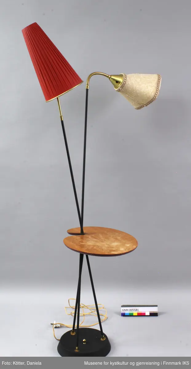 Stålampa har tre svarte stenger nede som er festet på en rund fot med messingbeslag. Stengene krysser hverandre nedenfor midten og et av dem ender som feste for et lite, nyreformet bordplate av finert og lakkert tre. To stenger fortsetter oppover og skrår utover. En av stengene avslutter rett og har et messingbeslag som står i kontrast til den røde, plisserte lampeskjermen av plast. Den andre stangen avslutter med et fleksibelt messingelement som holder det firkantede, beige-brune lampehodet med avrundede kanter av strukturert plast.  Den elektriske ledningen til lampa er festet under foten.