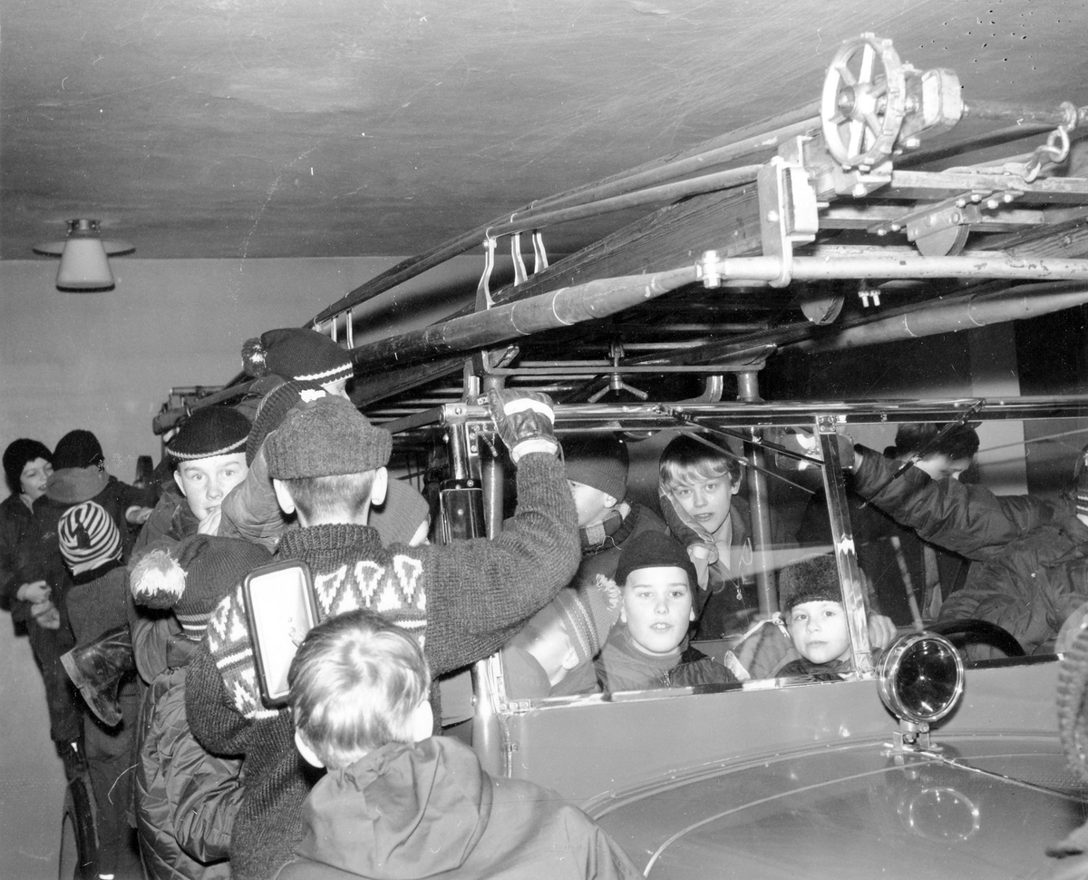 Brandkåren. Pojkar står vid och sitter i brandbil i Alingsås brandkårens garage på 1960-talet.