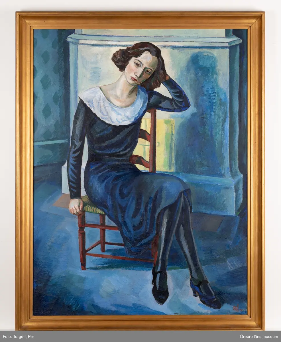 Kvinna sittande på en stol med huvudet lutat mot handen. I bakgrunden en kakelugn
Dominerande färg blå.