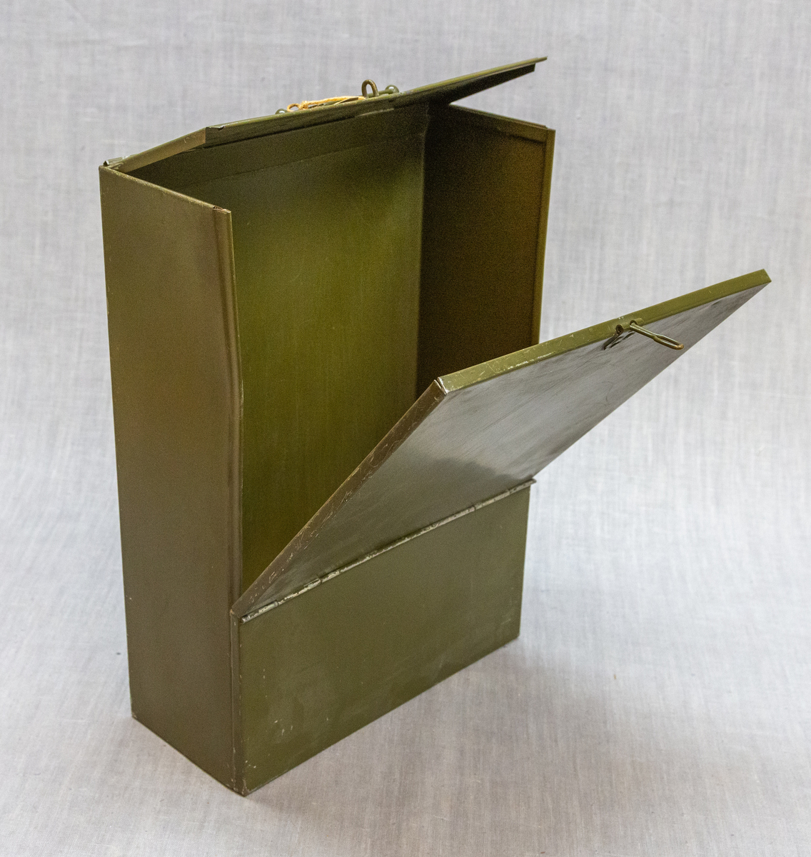 Rektangulær "militærgrøn" metallboks med ledda lokk, handtak for uttrekk frå hylle og metaløkker for feste av hengelås. 