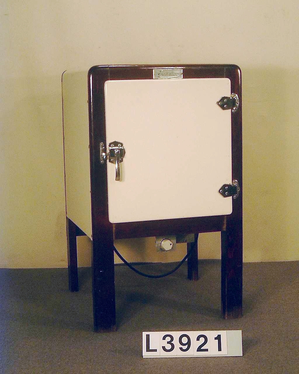 Fristående kylskåp typ L 15b med kylapparat typ 22 A. Värmedrivet, där ramen är i brunt trä och kabinettet är i emalj. Kromat dörrhandtag med stängningsfunktion. Ovanför dörren sitter en skylt med firmanamnet: Electrolux.