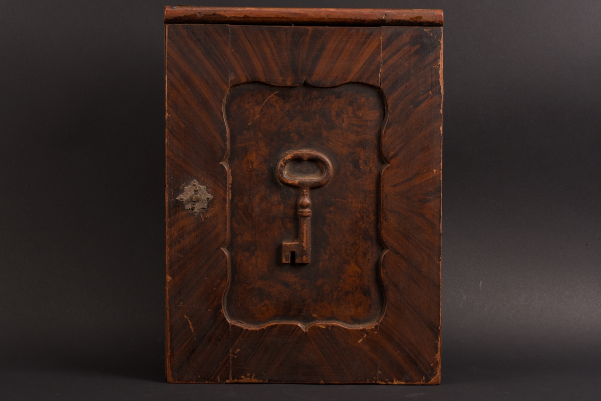 Rektangulärt nyckelskåp med vänsterhängd dörr av furu. På skåpsdörren är det en utsnidad nyckel. Skåpets utsida är målat i brun marmorering. Inne i skåpet tre böjda metalltenar för att hänga nycklarna på.
