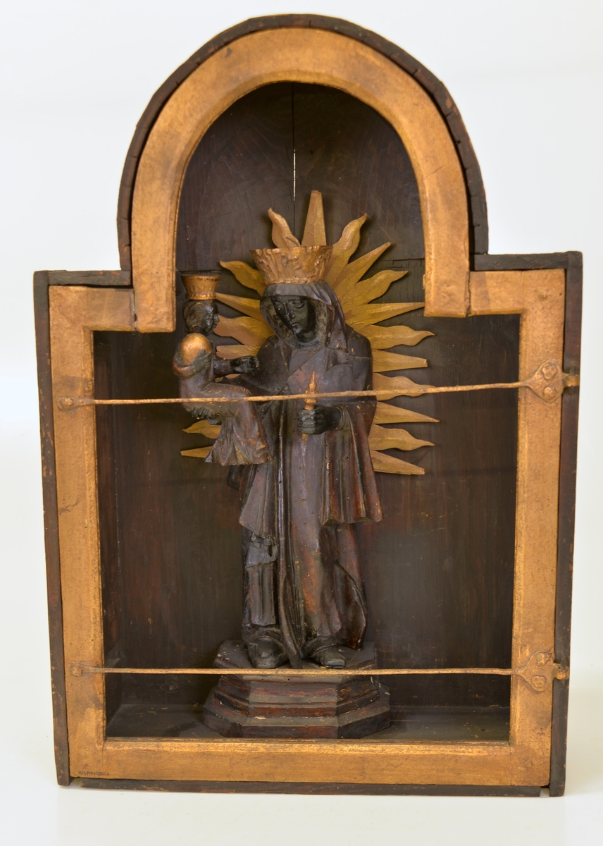 
Skåp av svartmålat trä. Skåpets dörr utgörs av en med gångjärn fäst ram, målad med guldfärg.
Madonna med Jesusbarn, skuren i trä. Båda figurerna med kronor målade i guldfärg och på profilerad fotplatta.
