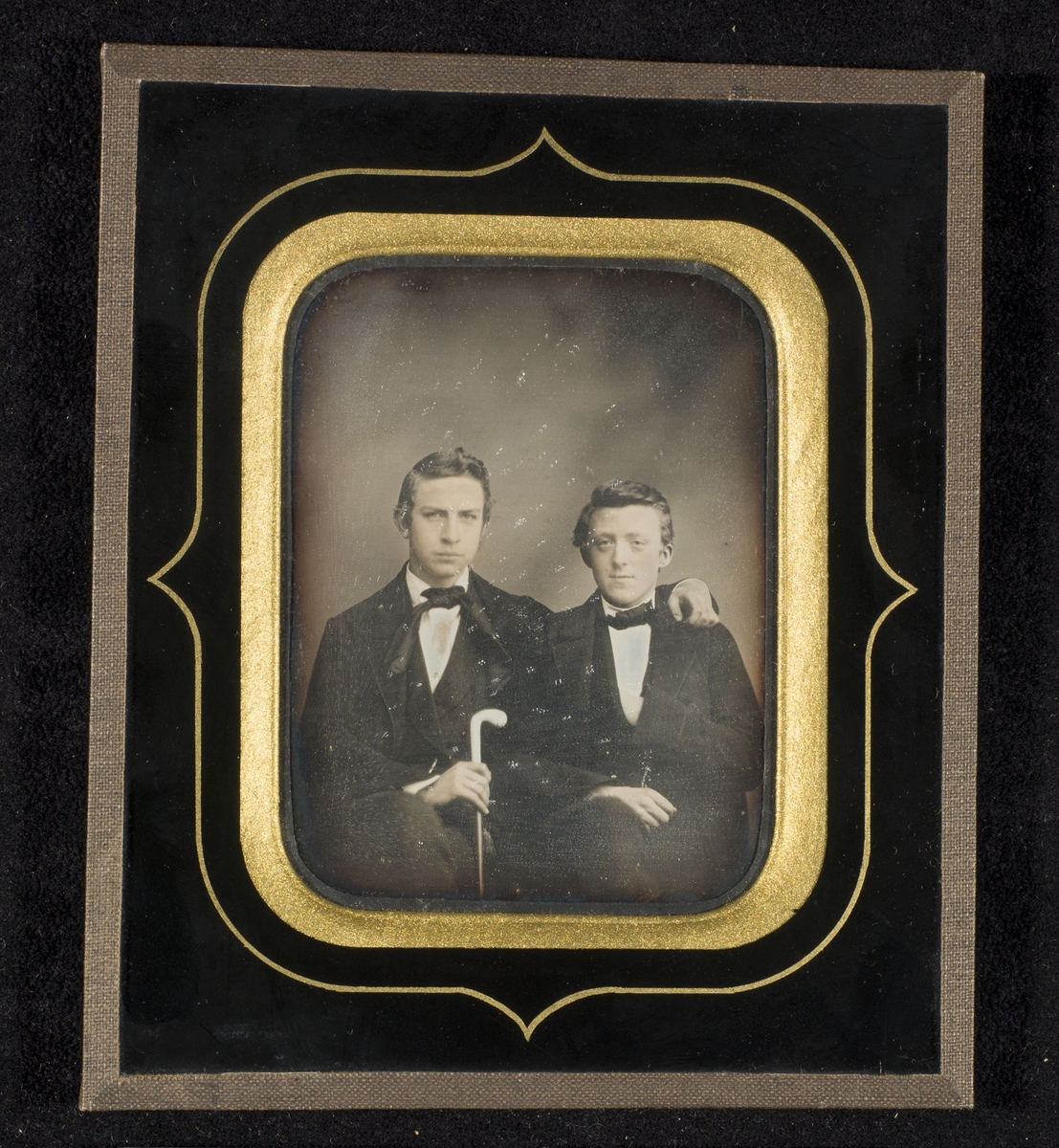Daguerreotypi av to unge menn sittende tett sammen.