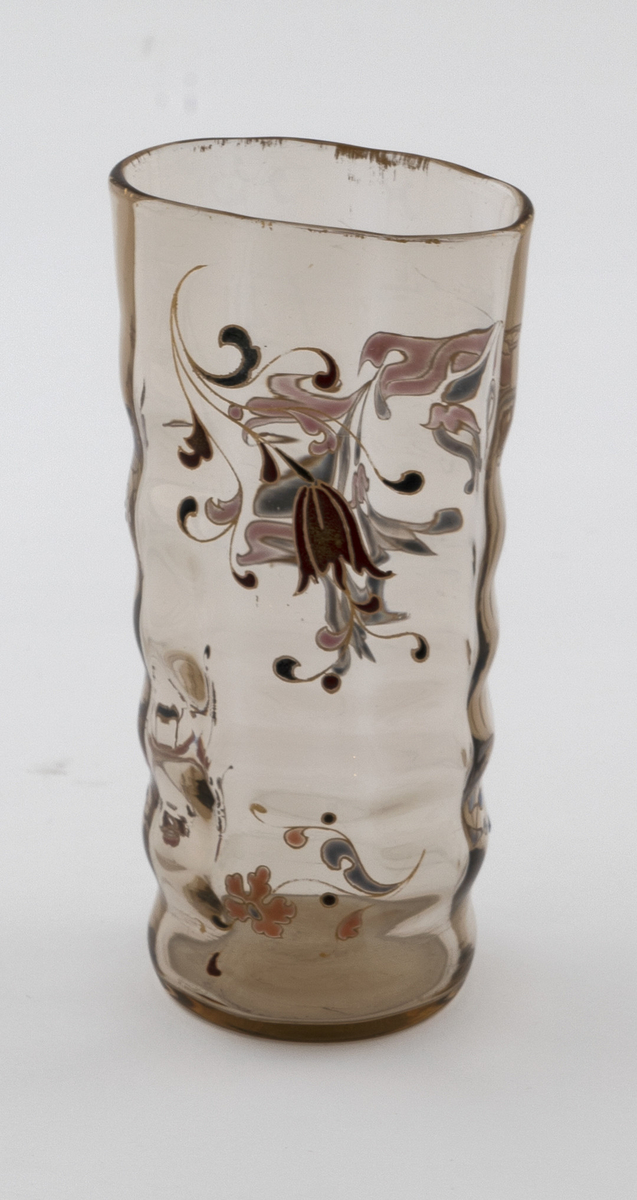 Begerformet vase i gjennomskinnelig glass med gulbrun fargetone. Lett bølgende vegger, som skaper en dynamisk bevegelse i vasens utforming. Sirkulær fot, som gradvis glir over i en ovalform på øvre del av korpus. Vasen avsluttes med en forgyllet munningskant. Korpus er dekorert med organiske motiver i emaljemaling. På den ene siden er blomster- og -grener primært fremstilt i burgund og sort, mens på den andre siden er de holdt i grått og rosa. Emaljemalingen innrammes av forgylte konturlinjer.