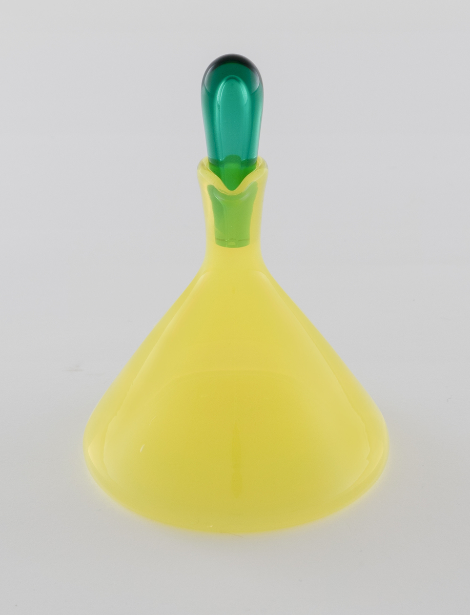 Edikk- eller oljekaraffel med propp i farget glass. Konisk koprus i halvgjennomskinnelig gulfarget glass, som avsluttes i en smal hals med tut. Den dråpeformede proppen er utført i gjennomskinnelig grønnfarget glass.