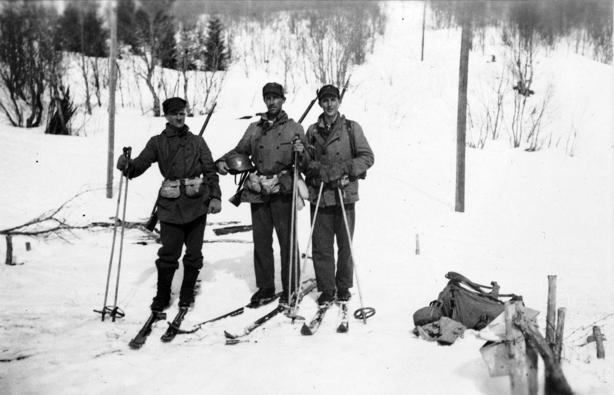 Tre norske soldater på ski. En av dem har har med seg en tysk hjelm.