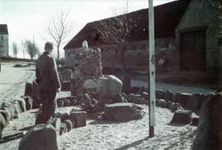 Soldat i tysk uniform ved et minnesmerke. Bygningen i til ve
