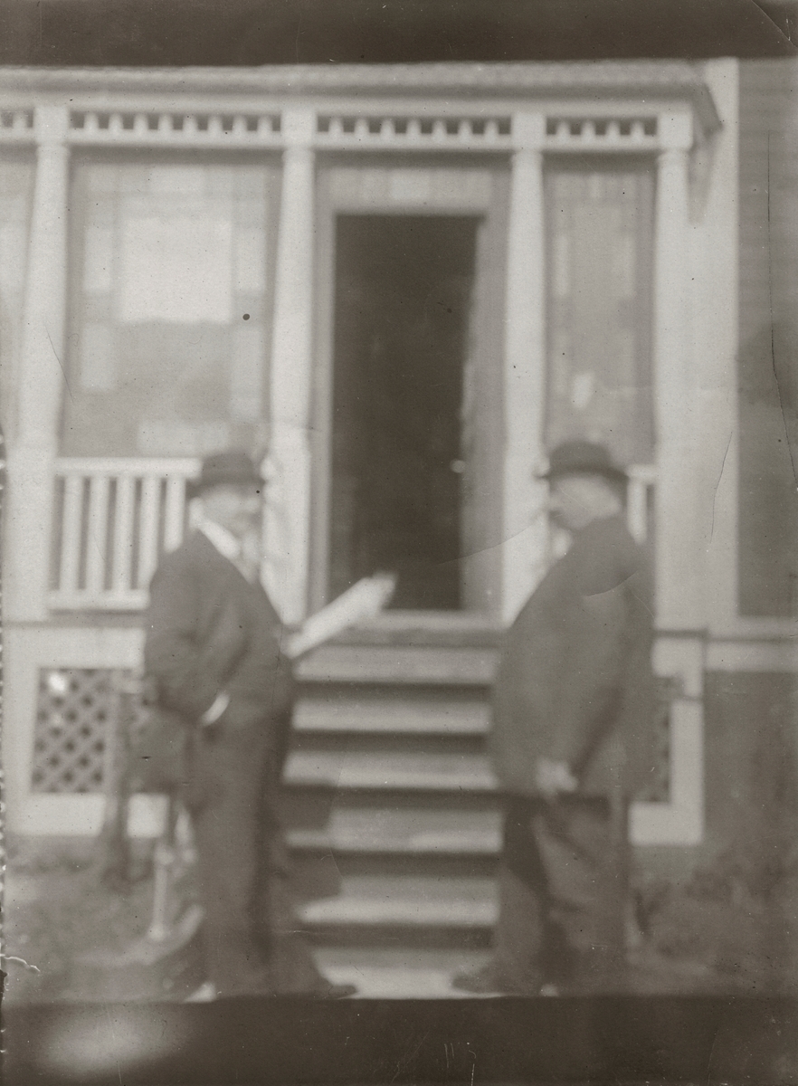 Portrett av to menn som står foran trappa til et hus.