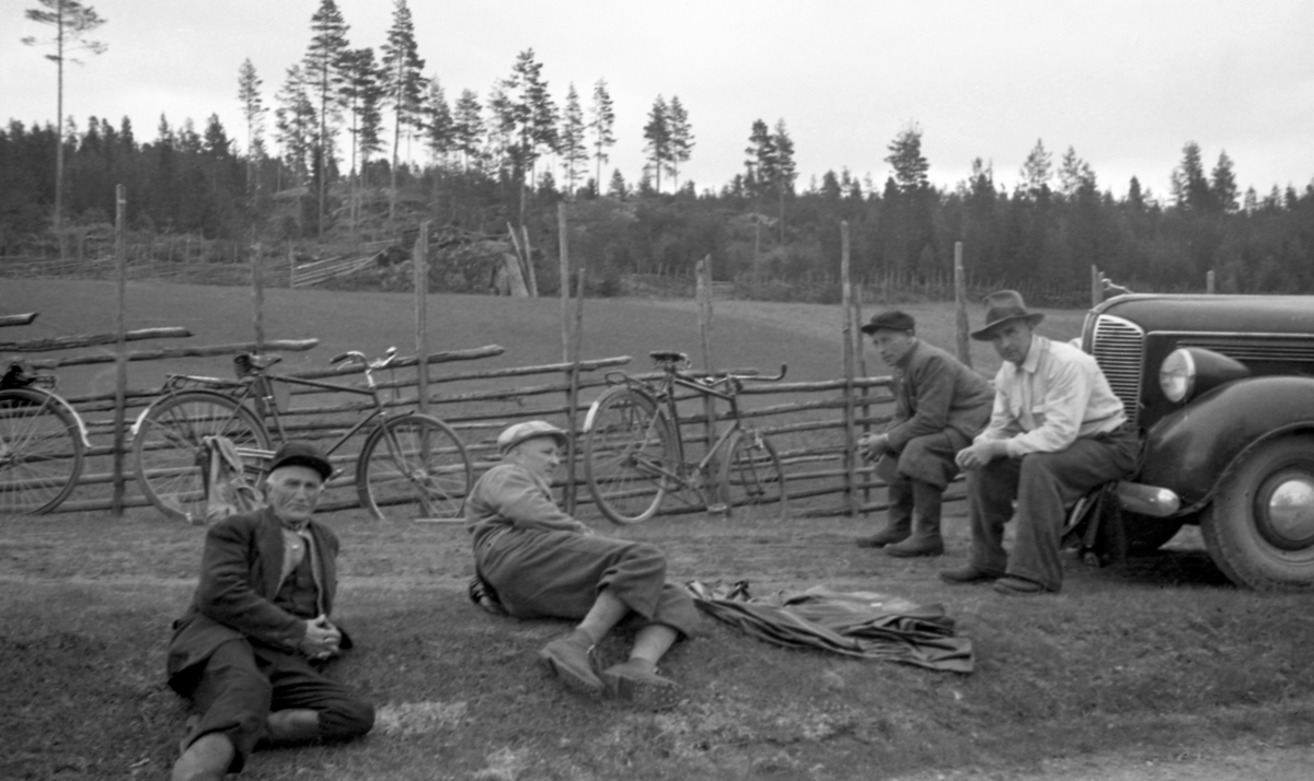 Fire personer tar en pust i bakken. 3 sykler. 1 bil. Gjerde. Åker. Fra venstre: Ikke navngitt, Kr. Halvorsen, O. Funi ? T. Øverby.