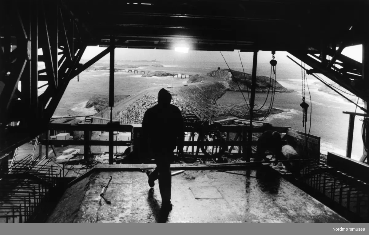 Fra byggingen av Atlanterhavsveien mellom Averøy og Eide i Møre og Romsdal. En veistrekning på 8.274 meter. Anlegget består av åtte broer på til sammen 891 meter og går over holmer og skjær. Veien kostet 122 millioner i 1989 og var delvis bompengefinansiert. Anlegget ble åpnet 7. juli 1989 og bommen ble fjernet i juni 1999. Atlanterhavsveien er landets åttende best besøkte naturbaserte turistattraksjon (2004) med 283.500 besøkende. Veistrekningen er foreslått vernet i "Nasjonal verneplan for veger, bruer og vegrelaterte kulturminner." (Kilde: Wikipedia Norge). Bildet er fra avisa Tidens Krav sitt arkiv i tidsrommet 1970-1994. Bildet er fra avisa Tidens Krav sitt arkiv i tidsrommet 1970-1994. Nå i Nordmøre museums fotosamling.
