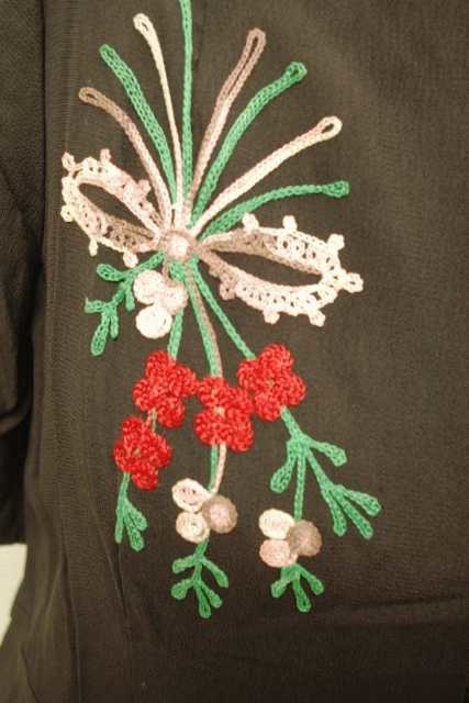 Kjolen har et broderi på den ene siden av livet, og korte ermer ned til albuen og skulderputer. Sort, rød, grønn og hvit.