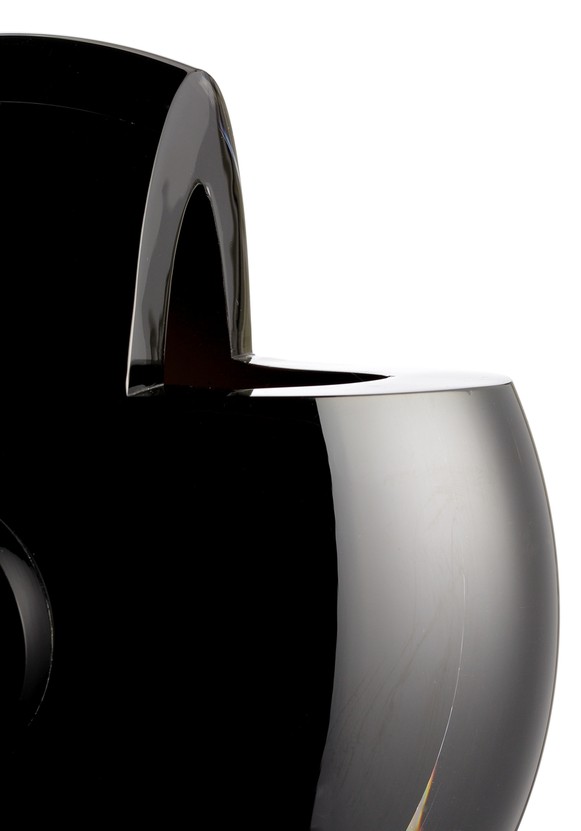 Design: Helen Krantz. Rund och flat skulptur i svart underfång med en större "knapp" på var sida. Vasens övre del har två 90-gradiga utsågningar.