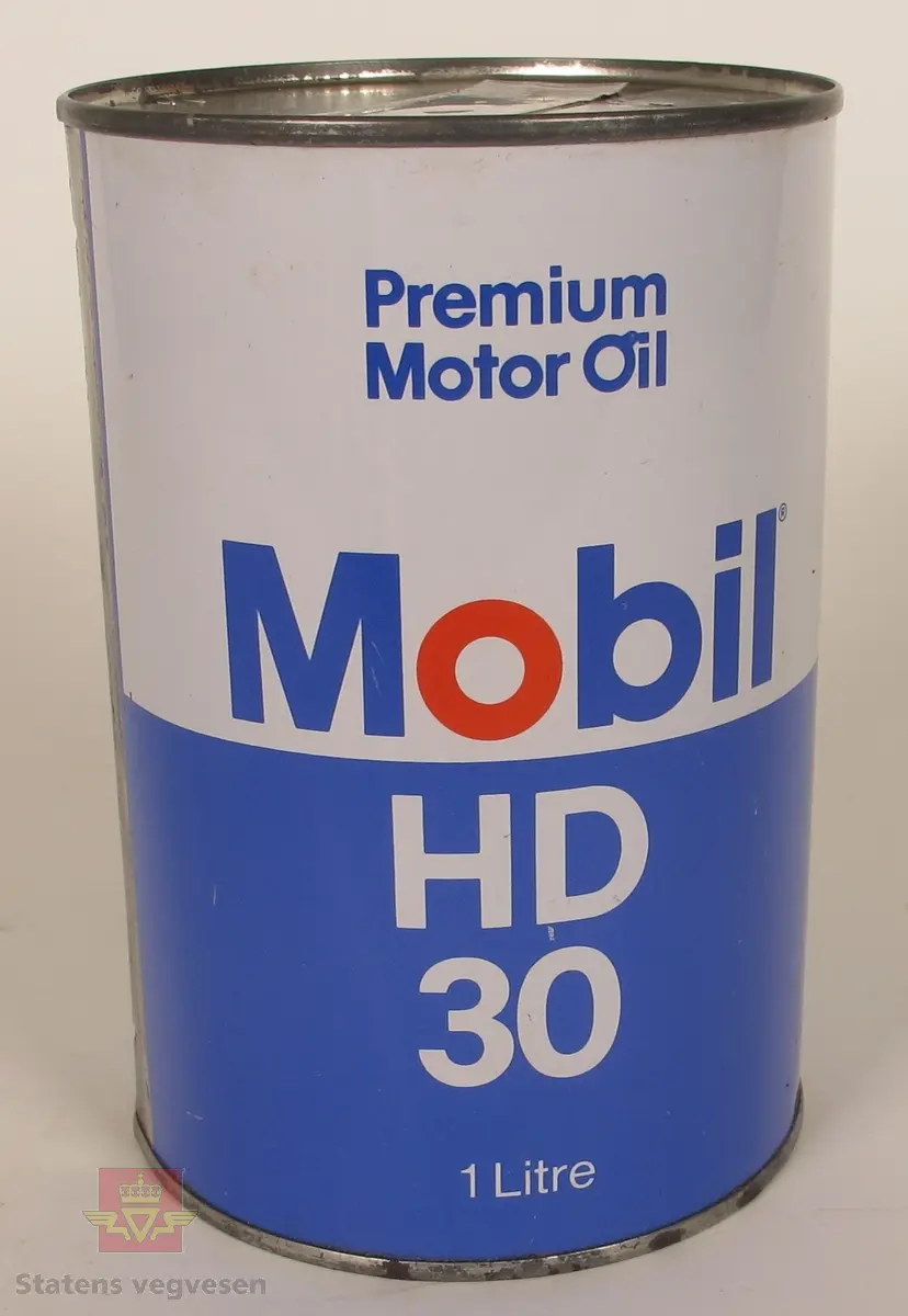 Sylinderformet boks i metall. Blå og hvit med skrift: Premium Motor Oil Mobil HD 30 1 litre på fremsiden. På baksiden er det skrift på engelsk og svensk.
