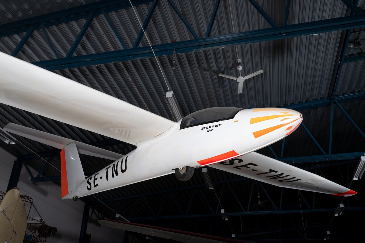 Segelflygplan av modell Pilatus B 4. Ensitsigt plan av plåt med vit flygkropp och vingar samt orange dekor.