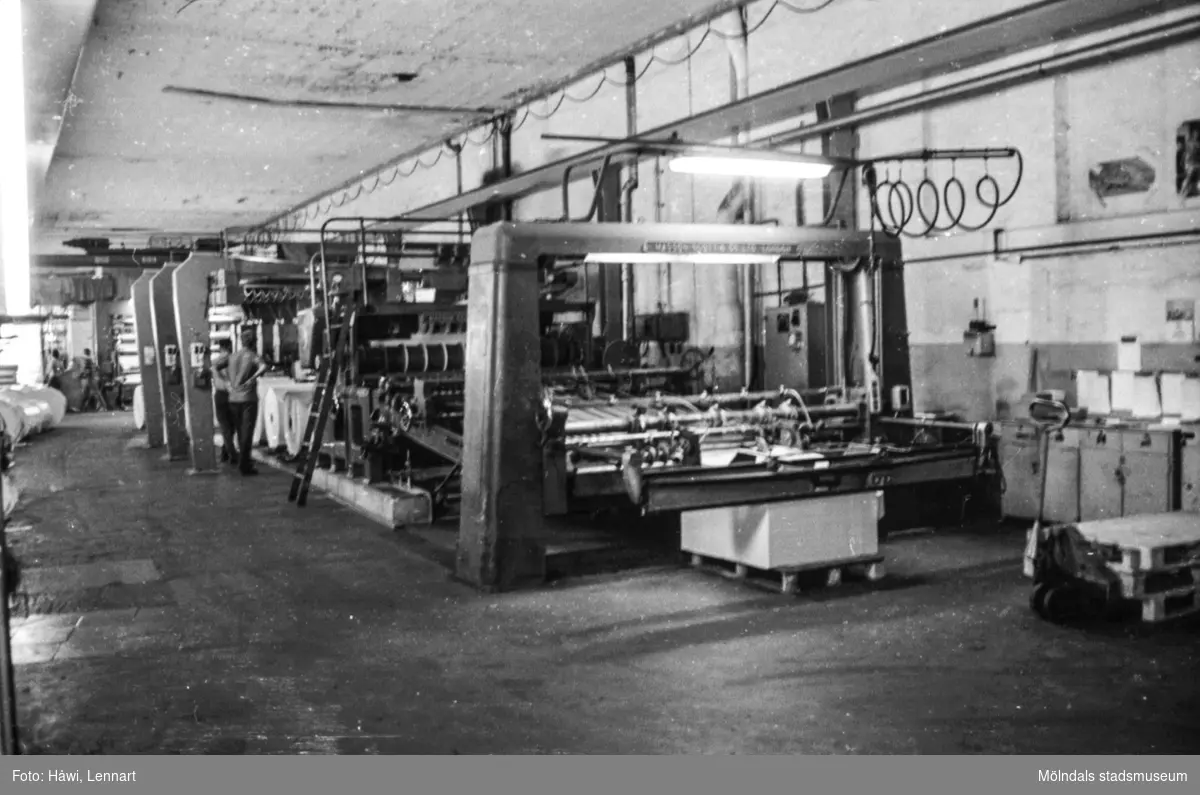 Män i arbete vid maskin. Klipp 5 och klippta pappersark på pall. Byggnad 10. Pappersbruket Papyrus i Mölndal, hösten 1970.