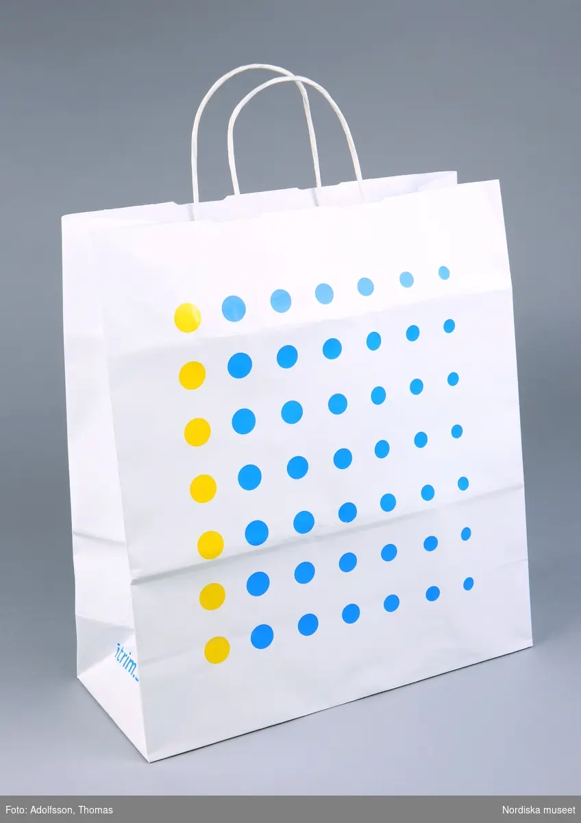 Inköpskasse, av vitt papper med å ena sidan Itrims logotyp, å andra sidan prickig dekor i gult och blått.