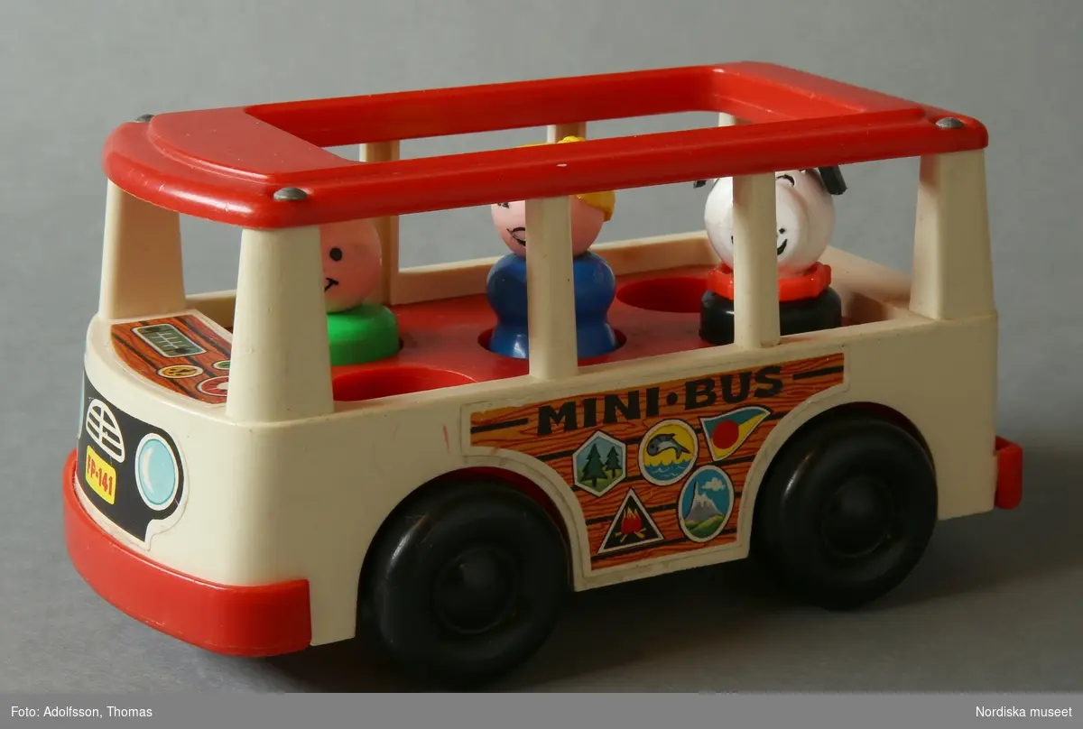 Minibuss, leksak av hårdplast tillverkad av Fisher Price, röd och vit, med 4 rörliga hjul. Metalldelar och masonitbotten. Inuti bussen finns fem hål för tillhörande figurer. Tre figurer placerade, en kvinna, en man och en hund.