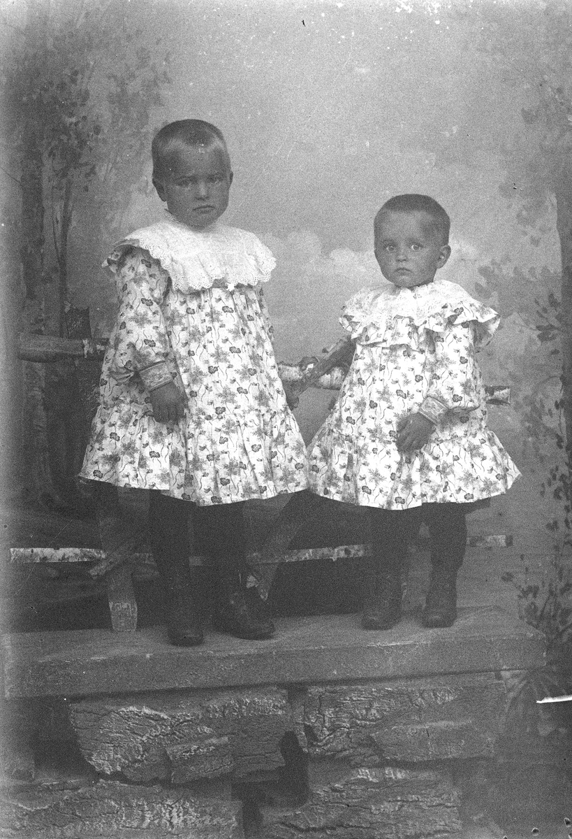To små jenter i lyse, blomstret kjoler m/hvite blondekrager.