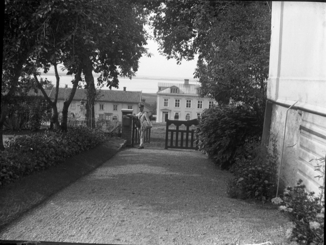 Från Borgmästargårdens trädgård ut mot torget. Vid den öppna grinden står sannolikt brevbäraren. På andra sidan torget syns bebyggelsen utmed Brahegatan.