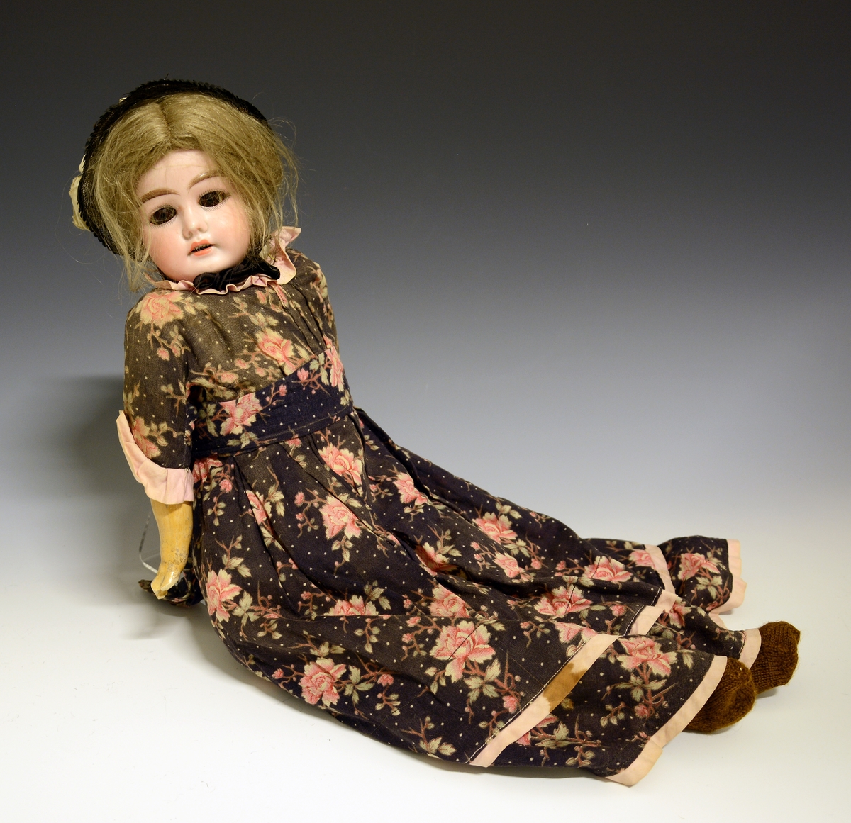 Dukke med kropp sydd av stoff, fylt med sagflis e.l. Armer og ben av gips. Hode av porselen (bisquit).