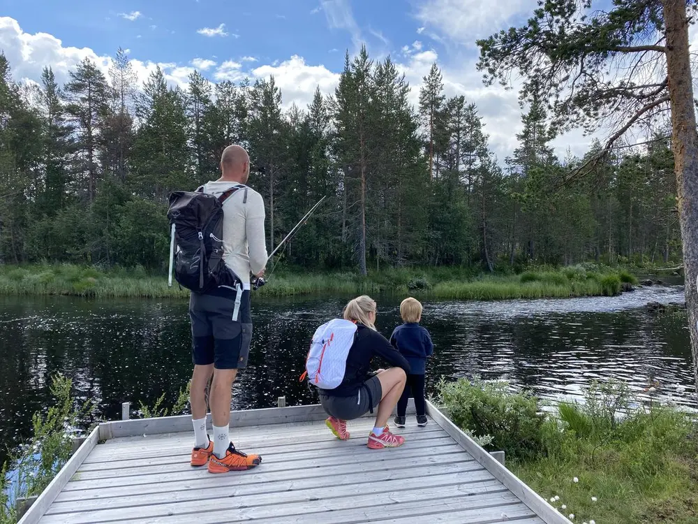 En familie fisker på kanten av en brygge ved en innsjø.