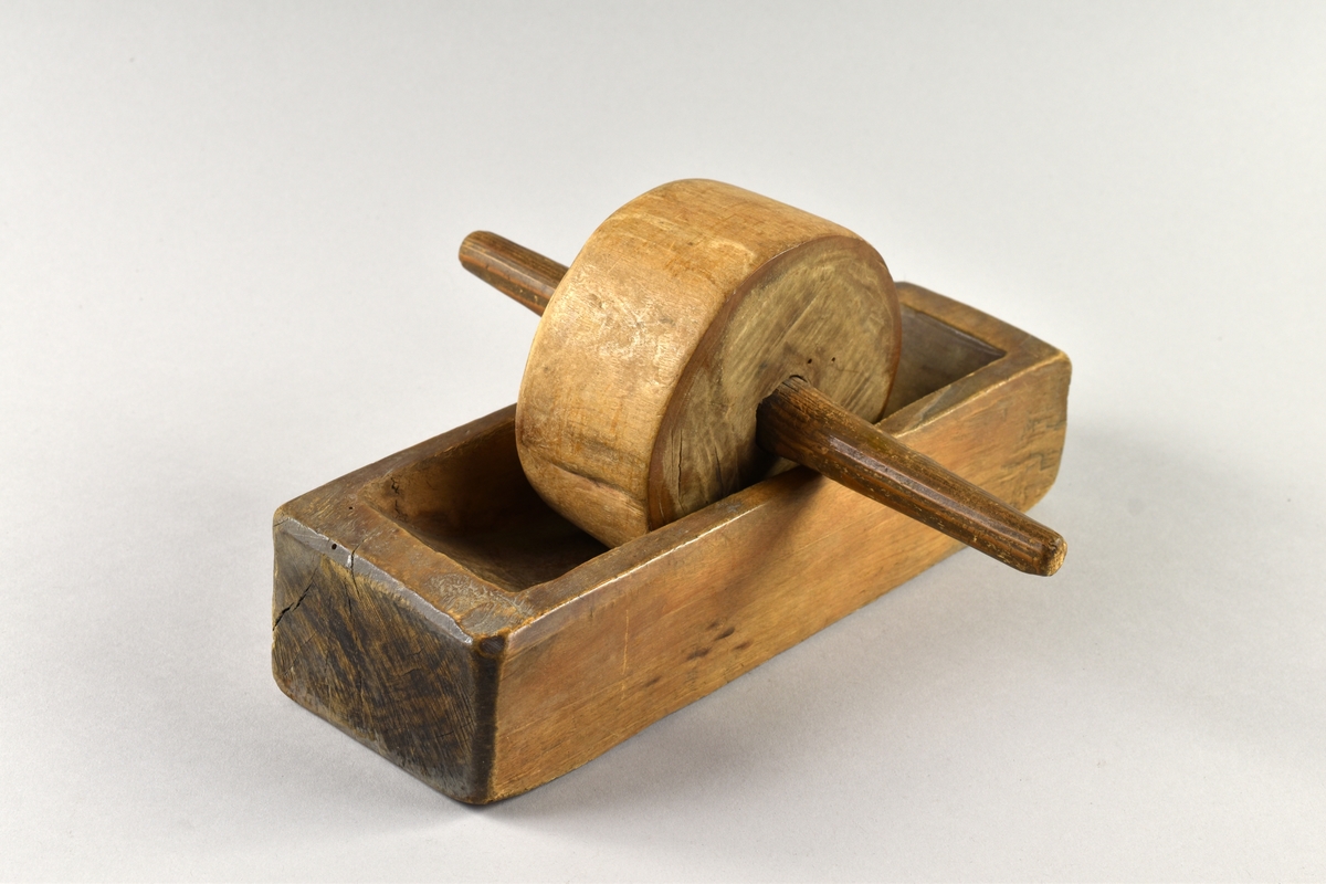Kaffekvarn av trä. Består av ett rektangulärt urkarvat tråg och en rulle (malhjul). I mitten på rullen en pinne.