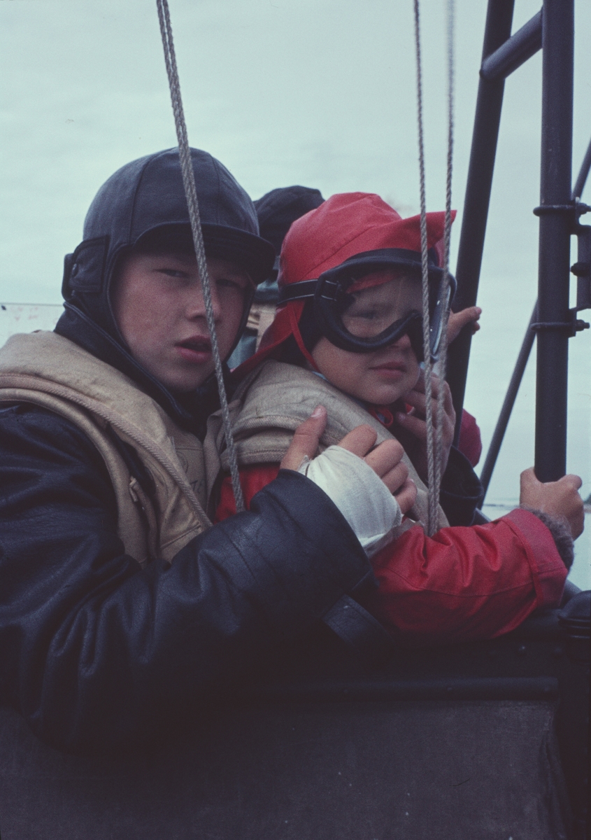Bilden visar två barn i skyddkläder ombord på en motortorpedbåt.