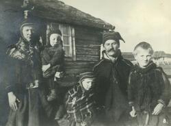 Ukjent samisk familie avbildet foran trehus med torv på take