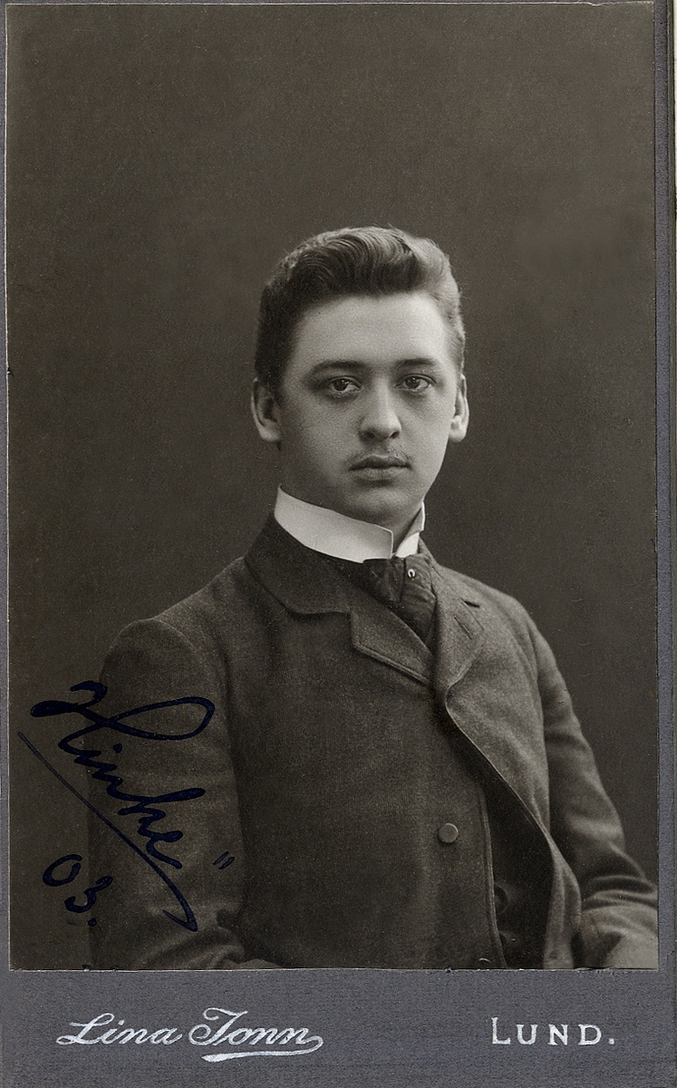 Porträttfoto av en man i kavajkostym med väst, stärkkrage och slips.
I nedre vänstra hörnet syns en autograf m.m.: "Hinke, 03". 
Midjebild, halvprofil. Ateljéfoto.