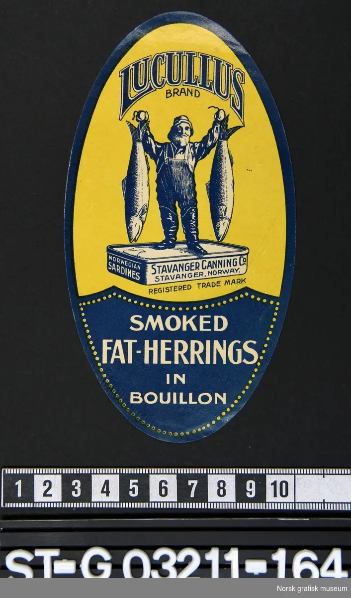 Oval etikett i gul, blå og hvit. Hovedmotiv er en fremstiling av en fisker stående på en overdimensjonert hermetikkboks mens han holder to store fisker. 

"Smoked fat- herrings in bouillon"