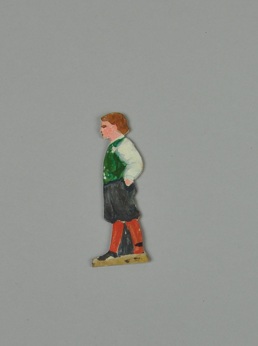 Figur av papp. Figuren forestiller gutt i sideprofil, med hendene i lommen. En annen del kan skyves over figuren, slik at gutten holder to bøtter. Figuren er malt på begge sider.
