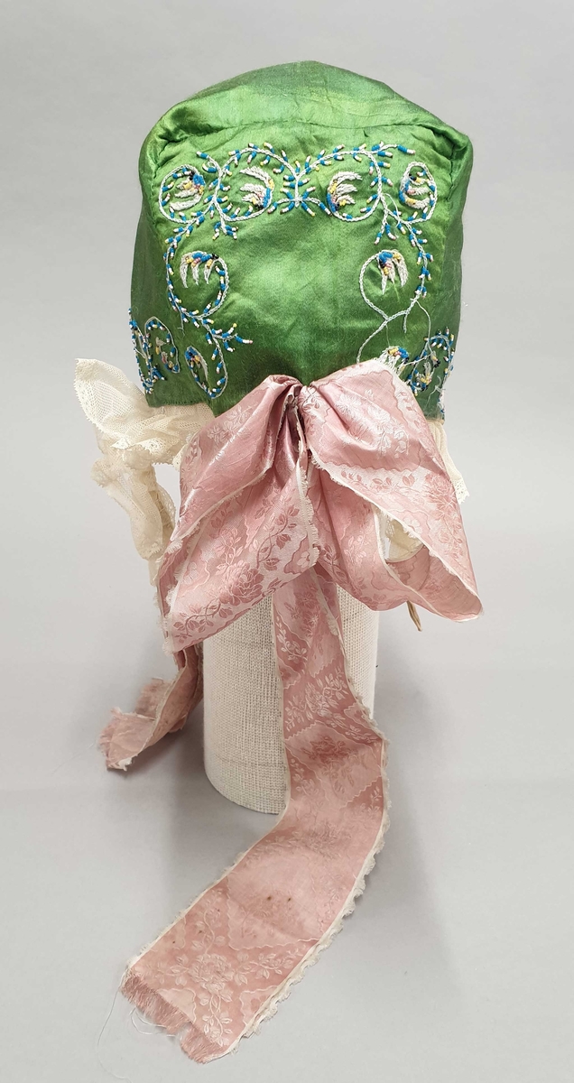 Grønn kyse av silke med brodering langs kantene og midt bak. Strimmel av hvit tyll og rosa silkesløyfe midt bak.