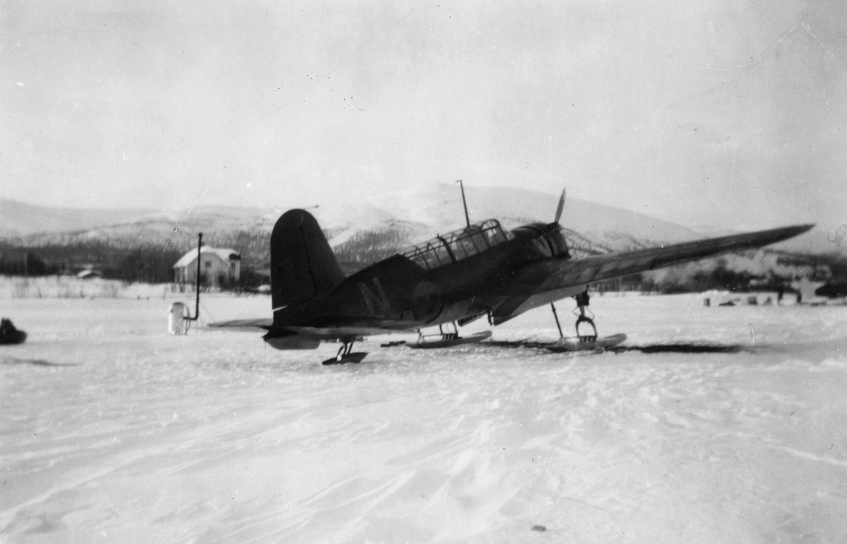 Flygplan Saab B 17 står på ett snötäckt fält i Gällivare, 1944. I bakgrunden syns fjället Dundret. Vy bakifrån. Under övning i Gällivare.