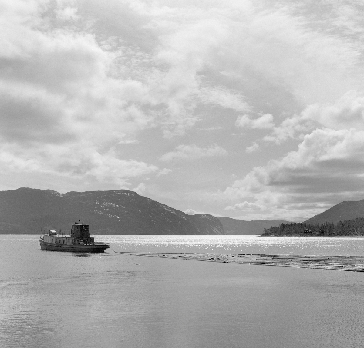 Slepebåt sleper tømmer over innsjø. Tømmersleping med slepebåten M/S Teisner på Fyresvatnet, Fyresdal, Telemark. Skipper Gunnar Sandvik . Båten ble bygd på Akers mekaniske verksted, og var opprinnelig en kombinert passasjer- og slepebåt fra 1876, Den fikk navnet M/S Teisner i 1913. Etterhvert ble det en ren slepebåt. Etter at tømmertransporten forsvant i 1971, ble båten tatt vare på av "Reiarlaget Teisners vener", men i 1990 ble båten dratt på land. Fyresvatn.