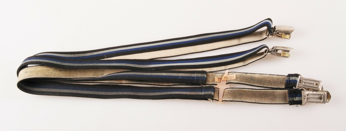 Selve selen er delt i to like deler, som består av et vevd elastisk "bånd", der gummistrikken er skjult i ripsveving med striper i svart, lys blå, blå og svart på retta, gråhvit på vranga. Hele lengden av "båndet" er ca 125 cm. I ene enden er det sydd fast en metallklype. Tilsvarende klype ligger i bukten av "båndet". Andre enden av "båndet" har en spenne festet fast og med spalte der "båndet" på "tilbakevei" er tredd gjennom. Her er det mulig å åpne spenna for regulering. De to seledelene trees i hver sin spalte i en rosa plast "spenne". Den er defekt.