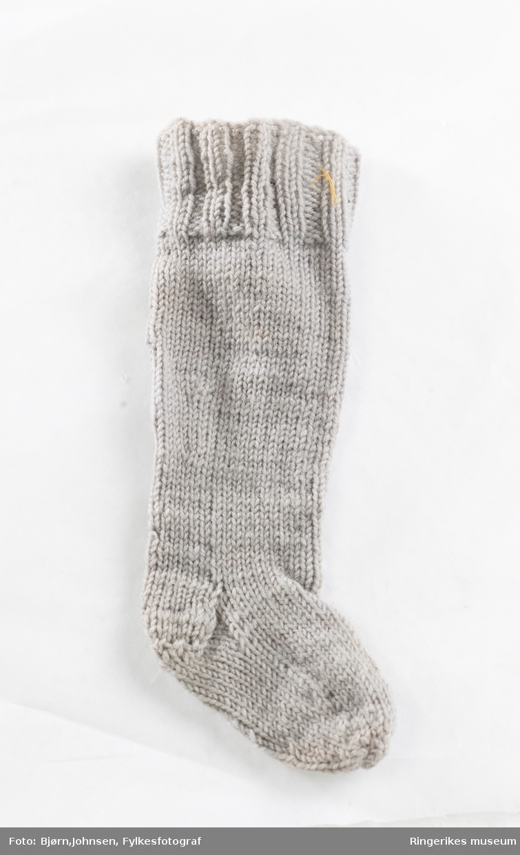 Dukketøy, strikket etter forbilde på strømper og sokker i voksen størrelse med vrangbord, hel- og tåfelling. Strikket på fem pinner med felling på leggen.