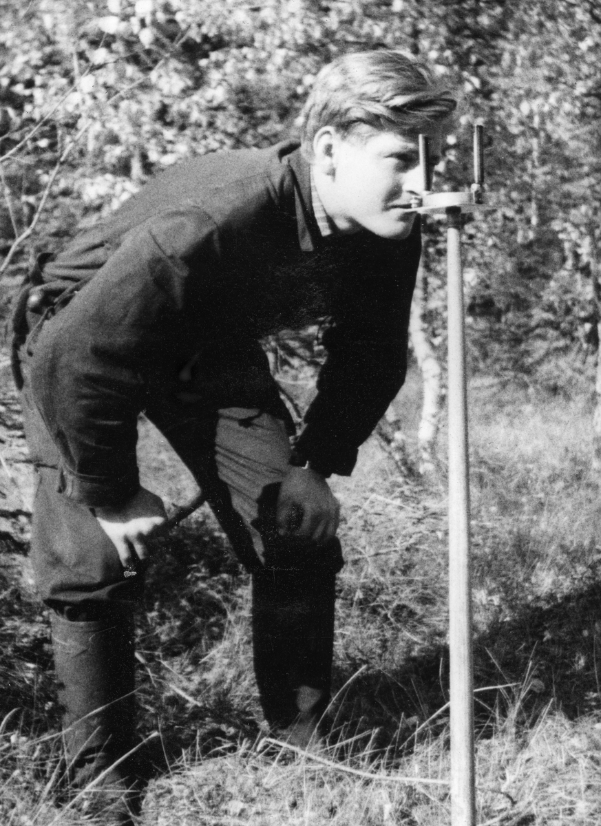 Nitten år gamle Knud Maartmann fra Gjøvik fotografert under takseringa av Opsal-skogene i Vardal i september 1940. Maartmann var kledd i dongeri og hadde langstøvler på beina. Han sto med bøyd overkropp og hendene på knærne, mens han sikter fra et kompass som står på en stake som er drevet ned i grasbakken.  Da dette fotografiet ble tatt var Maartmann i ferd med å ta fatt på et utdanningsløp som skulle gjøre ham til forstkandidat, og etter hvert til allmenningsbestyrer i Veldre almenning og Pihlske sameie i Ringsaker. 