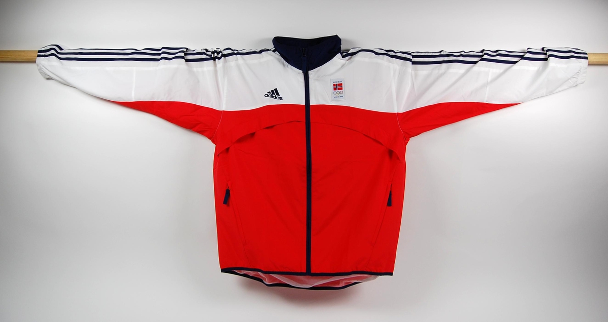 Rød, hvit og blå overtrekksdress bestånde av jakke og bukse. Dressen har logo for Olympic Team på ryggen, samt Adidaslogo på jakke og bukse. Det er påsydd et merke med det norske flagget, OL-ringene og innskriften ATHENS 2004 på brystet.